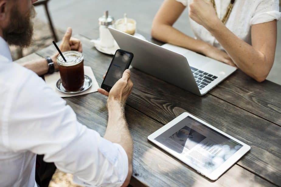 Geschäftsleute mit Laptop, Tablet und Handy am Tisch.