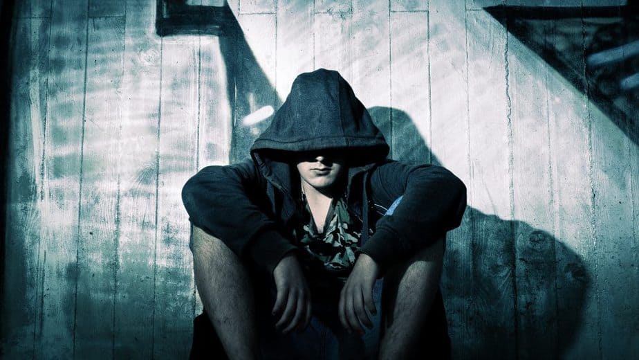 Mann mit Kapuze sitzt im Schatten